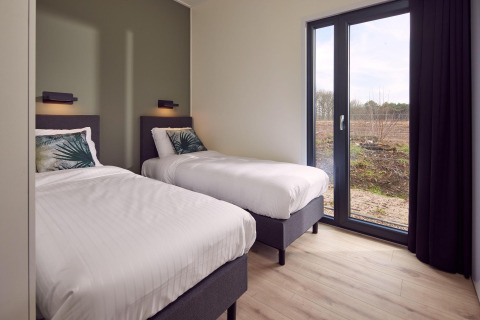 Modern twin bedroom in Water Lodge 6 Deluxe at Hofparken Wiltershaar, Netherlands, with natural outdoor view.