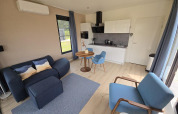 Modern living room with kitchenette in Water lodge 2, blue furniture, wood floor, AC and large windows.