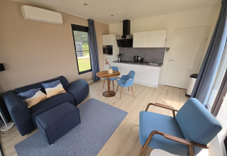 Moderne woonkamer met keukenhoek in Water lodge 2, blauwe zetels, houten vloer en grote ramen.