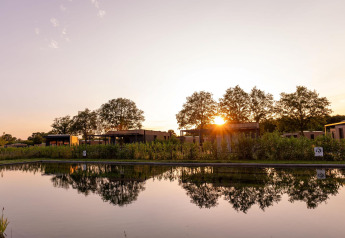 Atardecer sobre una cabaña junto a un estanque, cabañas modernas y árboles reflejados en el agua.