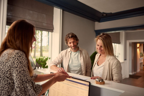 Par ved hotelreceptionen taler med receptionist under indtjekning på en hyggelig lodge om dagen.