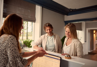 Koppel aan het onthaal van een lodge spreekt met de receptioniste tijdens het inchecken overdag.
