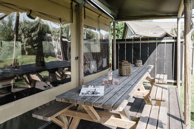 Covered outdoor seating at a lodge with rustic wooden table, benches, a wine bottle and two glasses.
