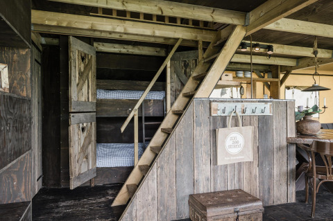 Interior de lodge acogedor con literas tras puertas de madera, escalera al altillo y comedor rústico.