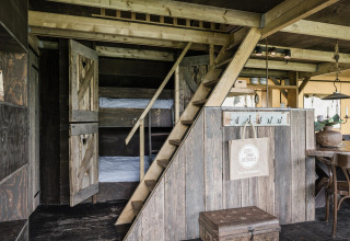 Interior de lodge acogedor con literas tras puertas de madera, escalera al altillo y comedor rústico.
