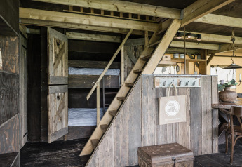 Ein rustikales Lodge-Interieur mit Holztreppe, Etagenbetten hinter Scheunentüren und Essbereich.