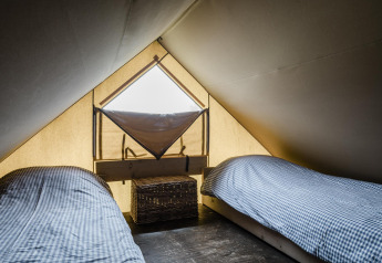 A cozy lodge room with two single beds with checkered bedding and a small window in the tent roof.