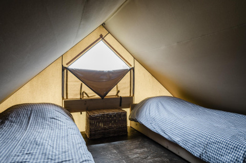 A cozy lodge room with two single beds with checkered bedding and a small window in the tent roof.