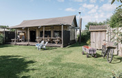 Bright lodge with a covered porch, picnic tables, outdoor chairs, bicycle, and wagon on a green lawn.