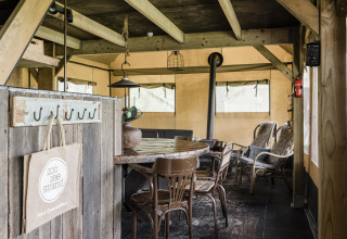 Interior rústico de una cabaña con mesa de madera, sillas y estufa en ambiente acogedor tipo tienda.