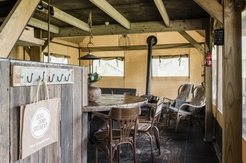 Interior rústico de una cabaña con mesa de madera, sillas y estufa en ambiente acogedor tipo tienda.