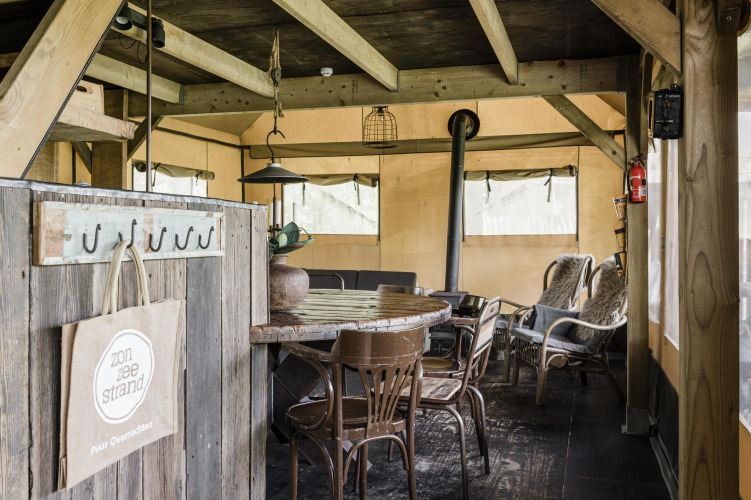 Rustic lodge interior with a wooden table, chairs, stove, and cozy seating area inside a tent-like room.