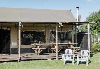 Outdoor view of a lodge with a covered porch, two picnic tables, and two white chairs on the grass lawn.