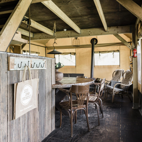 Interno lodge accogliente con mobili rustici in legno, stufa, sedie di vimini e atmosfera calda.