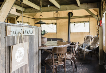 Intérieur de lodge avec meubles en bois rustiques, poêle, fauteuils en osier et ambiance chaleureuse.