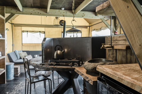 Cocina rústica y sala de estar en una cabaña, con muebles de madera, estufa de gas y sofá cómodo al fondo.