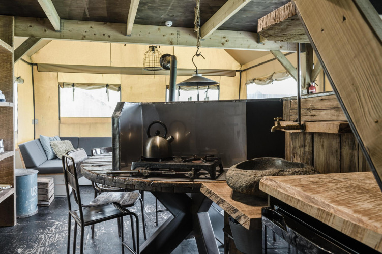 Rustic kitchen and lounge area inside a lodge, featuring wooden furniture, gas stove, and cozy sofa.