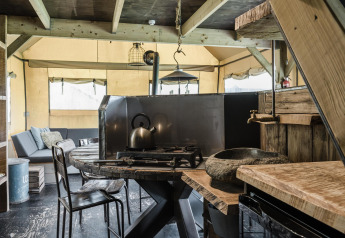 Cocina rústica y sala de estar en una cabaña, con muebles de madera, estufa de gas y sofá cómodo al fondo.