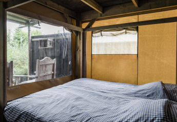 Intérieur d'un lodge confortable avec lit double, housse à carreaux et vue sur la nature extérieure.
