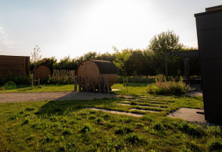 Zona exterior en un lodge con saunas en forma de barril, césped, terraza y sol poniente.