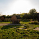Buitenruimte bij een lodge met tonvormige sauna’s, grasveld, terras en een ondergaande zon.