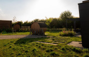 Lodge outdoor area with barrel saunas, green grass, patio seating, and the sun setting in the background.
