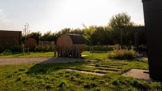 Lodge outdoor area with barrel saunas, green grass, patio seating, and the sun setting in the background.