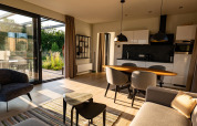 Modernes Lodge-Wohnzimmer mit offener Küche, großen Fenstern, Esstisch und viel Tageslicht.