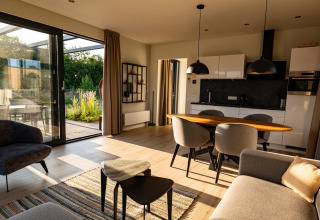 Moderne lodge-stue med åbent køkken, store vinduer, spisebord og masser af naturligt lys.