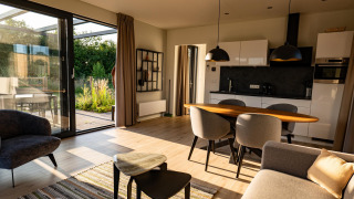 Modernes Lodge-Wohnzimmer mit offener Küche, großen Fenstern, Esstisch und viel Tageslicht.