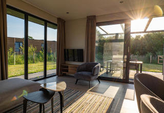 Salón moderno de lodge con grandes ventanales, luz solar y vistas al jardín y terraza exterior.