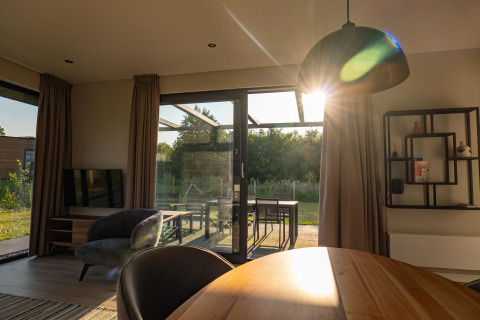 La luz del sol entra por puertas de cristal en una lodge moderna con vista a jardín y decoración elegante.
