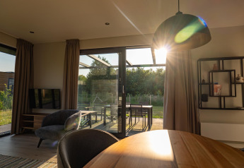 Sonnenlicht fällt durch Glastüren in eine moderne Lodge mit stilvollem Interieur und Gartenblick.