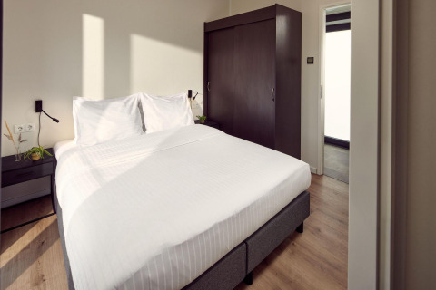 Habitación de lodge moderna con cama doble, sábanas blancas, armario oscuro y luz natural.