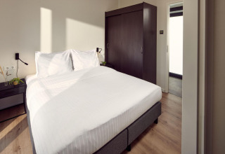 Habitación de lodge moderna con cama doble, sábanas blancas, armario oscuro y luz natural.