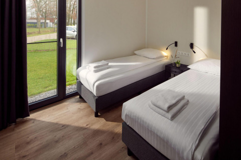Habitación luminosa de lodge con dos camas individuales, sábanas blancas y ventanas con vista al jardín.