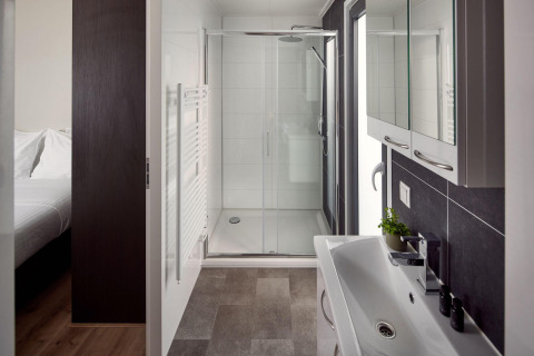Baño moderno y elegante en una cabaña con ducha, lavabo y armarios con espejo, visto desde el dormitorio.