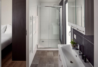 Baño moderno y elegante en una cabaña con ducha, lavabo y armarios con espejo, visto desde el dormitorio.