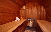 Wooden sauna at a lodge, featuring benches, towels, a wooden bucket, and a modern heater in the center.