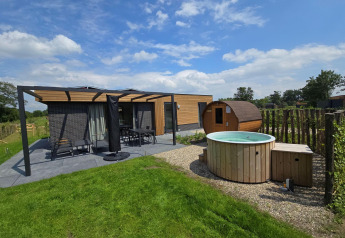 Buitenfoto van een moderne lodge met terras, tuinmeubilair, een tonvormige sauna en ronde hottub.