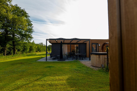 Foto de un lodge moderno con terraza, rodeado de césped verde y árboles bajo un cielo despejado.