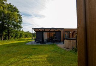 Foto de un lodge moderno con terraza, rodeado de césped verde y árboles bajo un cielo despejado.
