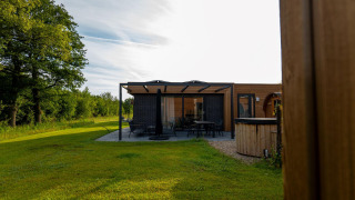 Foto einer modernen Lodge mit Terrasse, umgeben von grünem Rasen und Bäumen unter klarem Himmel.