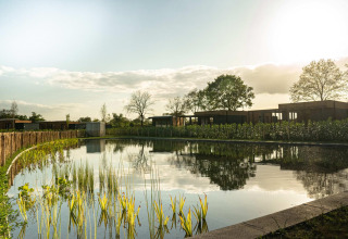 Un tranquilo lodge con cabañas modernas, un gran estanque y vegetación bajo la luz del atardecer.
