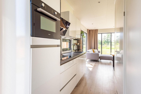Cocina moderna de lodge con horno, microondas y sala con sofá y ventanales que dan a la naturaleza.
