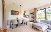 Lyst og moderne lodge-interiør med spisebord, sofa og store vinduer med udsigt til haven.