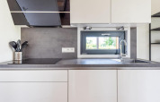 Cocina moderna con gabinetes blancos, fregadero, encimera negra y ventana con vista a la naturaleza.