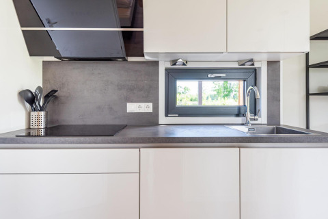 Cuisine moderne avec placards blancs, évier, plaque de cuisson et fenêtre donnant sur la verdure.