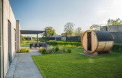 Lodge moderno con sauna de madera en el jardín, comedor exterior y vegetación bajo un día soleado.