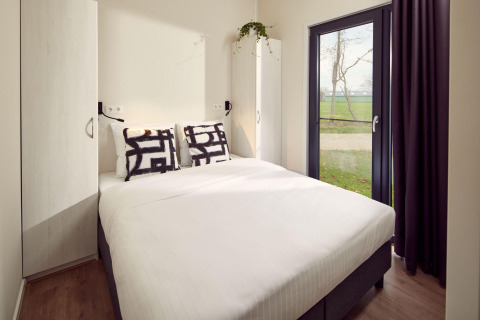 Dormitorio de lodge moderno con cama doble, armarios, cojines decorativos y gran ventanal al exterior.
